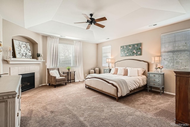 bedroom with a raised ceiling, a fireplace, carpet, a ceiling fan, and visible vents