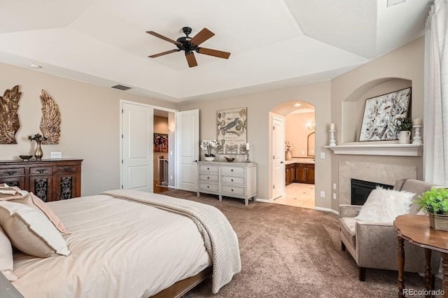 bedroom featuring visible vents, arched walkways, a fireplace, a raised ceiling, and carpet flooring