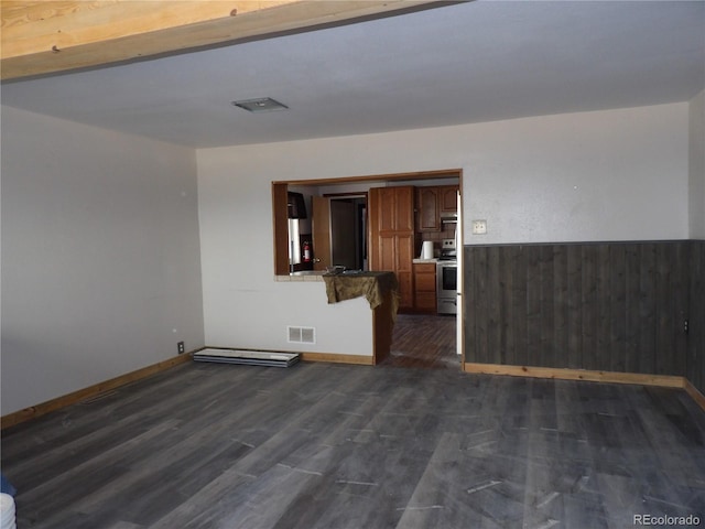 spare room featuring dark wood-style floors, a wainscoted wall, wood walls, and visible vents