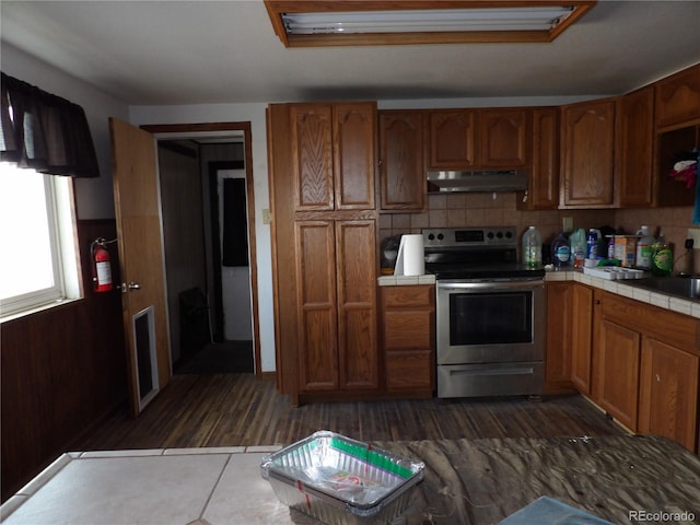 kitchen featuring electric range, brown cabinets, under cabinet range hood, backsplash, and tile countertops