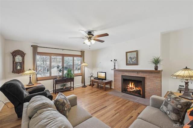 living room with a brick fireplace, ceiling fan, and light wood-type flooring