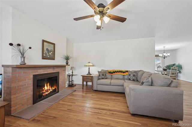 living room with ceiling fan with notable chandelier, a fireplace, and light wood-type flooring