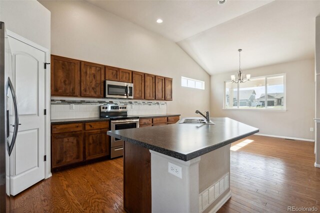 kitchen featuring stainless steel appliances, lofted ceiling, dark countertops, dark wood finished floors, and decorative backsplash