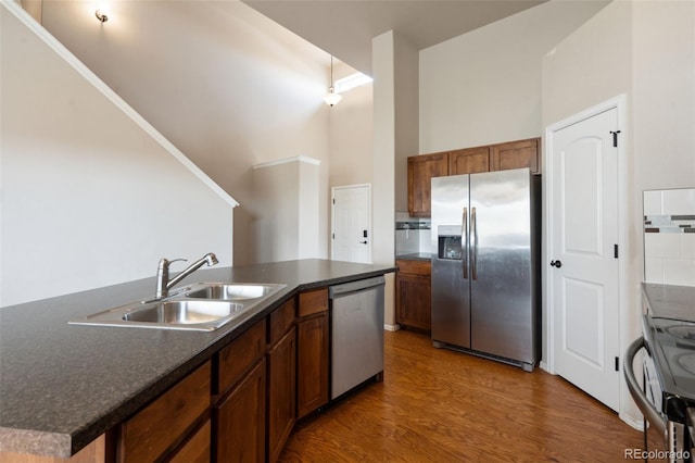 kitchen featuring appliances with stainless steel finishes, dark countertops, wood finished floors, a towering ceiling, and brown cabinets