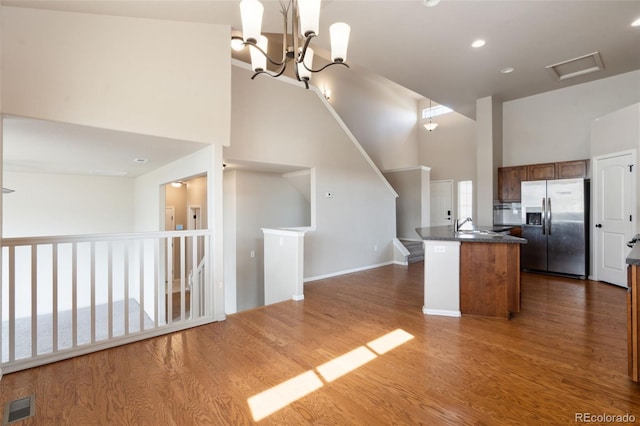 kitchen with stainless steel fridge with ice dispenser, a high ceiling, dark countertops, wood finished floors, and open floor plan