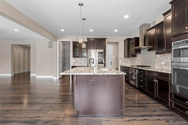 kitchen featuring a center island with sink, hanging light fixtures, light stone countertops, appliances with stainless steel finishes, and dark brown cabinets