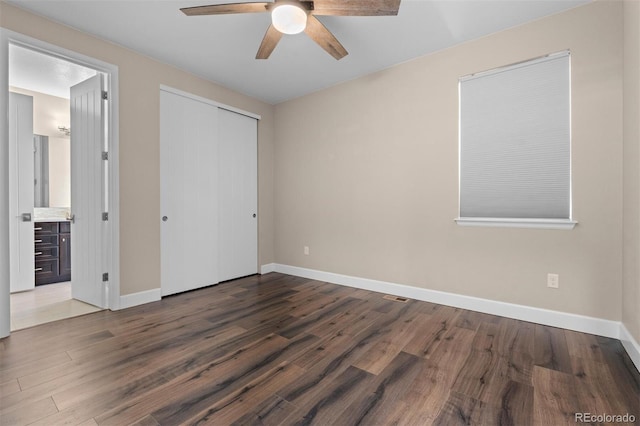 unfurnished bedroom featuring ceiling fan, dark hardwood / wood-style flooring, ensuite bath, and a closet