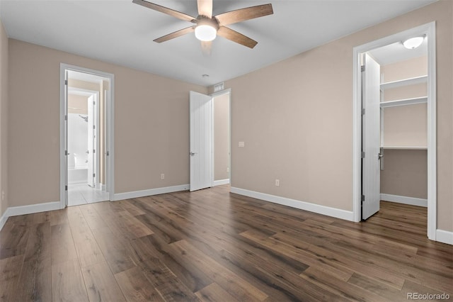 unfurnished bedroom featuring ensuite bath, ceiling fan, dark wood-type flooring, a spacious closet, and a closet