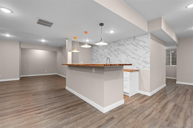 kitchen with hardwood / wood-style floors, wood counters, a kitchen breakfast bar, decorative light fixtures, and white cabinetry