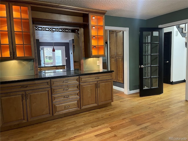 12381 E Vassar Dr, Aurora, CO 80014 - kitchen featuring light wood-style flooring, dark countertops, baseboards, glass insert cabinets, and a textured ceiling