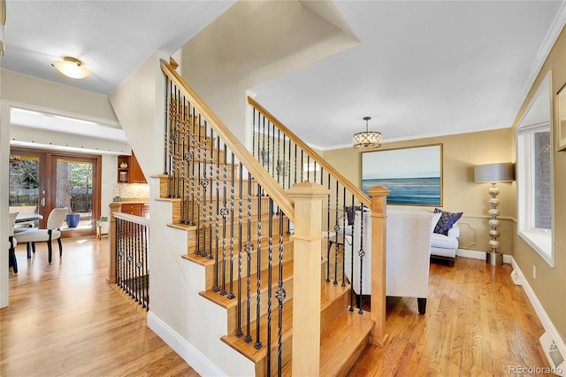 stairs with ornamental molding, an inviting chandelier, baseboards, and wood finished floors