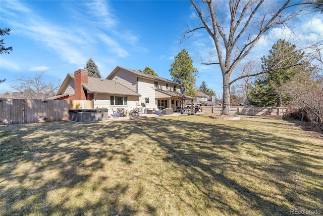 back of property featuring a patio area, a hot tub, a chimney, and a lawn