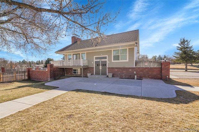 rear view of property with a chimney, fence, a yard, a patio area, and brick siding