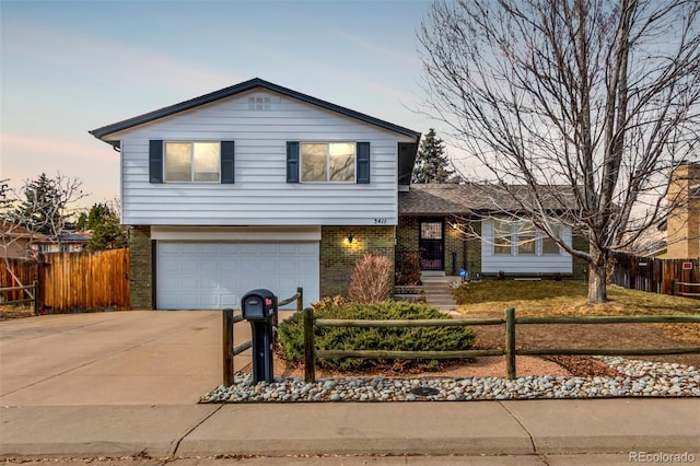 tri-level home featuring a fenced front yard, brick siding, driveway, and an attached garage