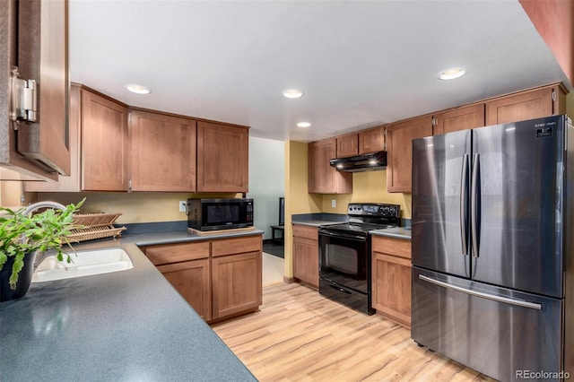 kitchen featuring light wood-style flooring, brown cabinets, under cabinet range hood, black appliances, and recessed lighting