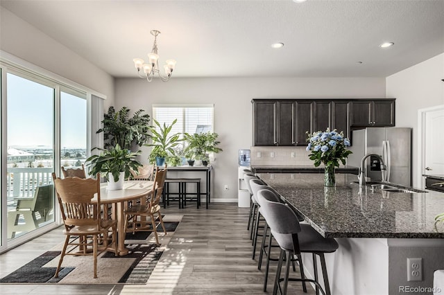 kitchen with sink, stainless steel fridge, dark hardwood / wood-style flooring, dark stone counters, and hanging light fixtures