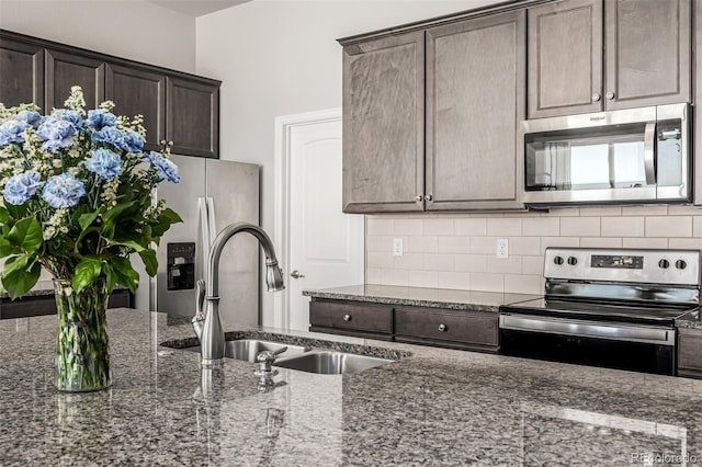 kitchen featuring dark brown cabinetry, appliances with stainless steel finishes, sink, and dark stone countertops