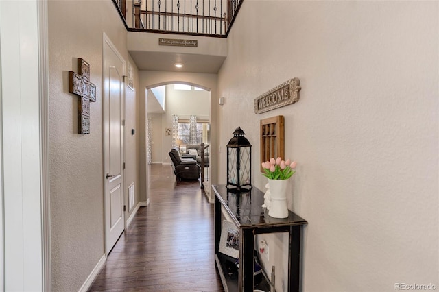 corridor featuring baseboards, visible vents, a high ceiling, arched walkways, and dark wood-type flooring