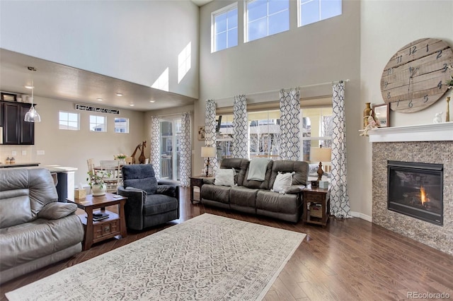 living room with a glass covered fireplace, dark wood-style floors, baseboards, and a healthy amount of sunlight