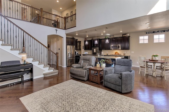 living room featuring stairs, baseboards, arched walkways, and dark wood-style flooring