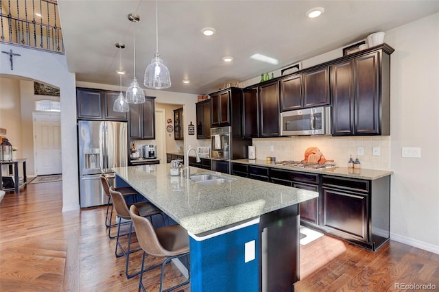 kitchen with a breakfast bar, arched walkways, a sink, dark brown cabinetry, and appliances with stainless steel finishes