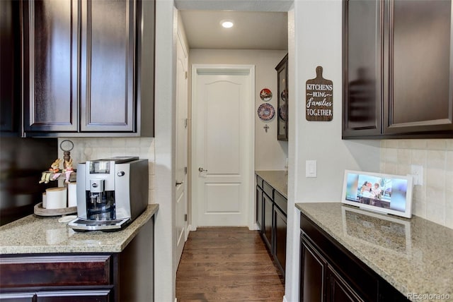 kitchen with dark brown cabinetry, decorative backsplash, dark wood finished floors, and light stone counters