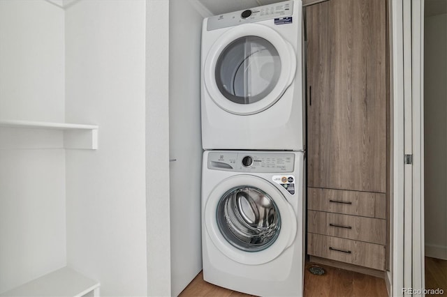 clothes washing area with hardwood / wood-style flooring and stacked washing maching and dryer