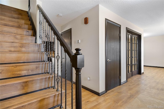 staircase featuring a textured ceiling, baseboards, and wood finished floors