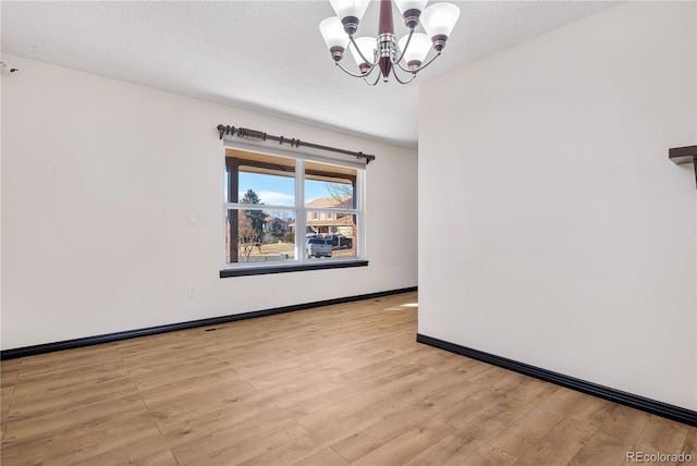 unfurnished room with light wood-type flooring, baseboards, a chandelier, and a textured ceiling