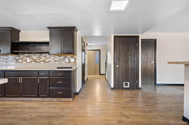 kitchen featuring light wood-style flooring, baseboards, dark brown cabinets, backsplash, and open shelves