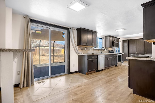 kitchen with dark brown cabinetry, visible vents, backsplash, stainless steel appliances, and a sink