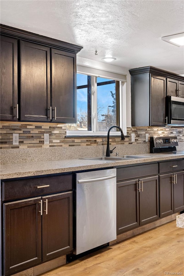 kitchen with stainless steel appliances, backsplash, light wood-style flooring, a sink, and dark brown cabinets