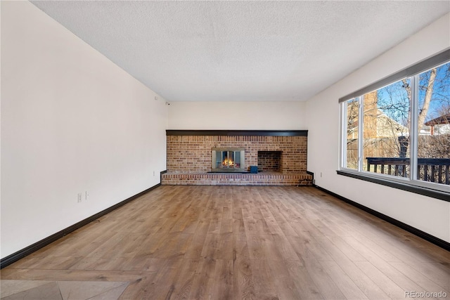 unfurnished living room with a textured ceiling, a fireplace, baseboards, and wood finished floors