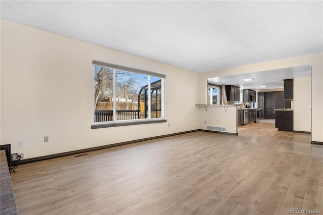 unfurnished living room with light wood-style floors, visible vents, and baseboards