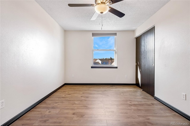 unfurnished room featuring light wood-type flooring, ceiling fan, a textured ceiling, and baseboards