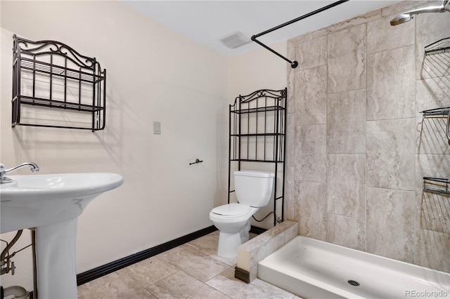 bathroom featuring toilet, a sink, baseboards, and tiled shower