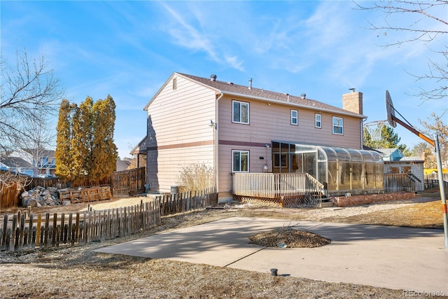 rear view of house with a deck, driveway, a chimney, and fence private yard