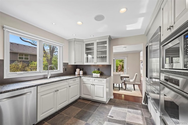 kitchen with a sink, recessed lighting, backsplash, glass insert cabinets, and appliances with stainless steel finishes