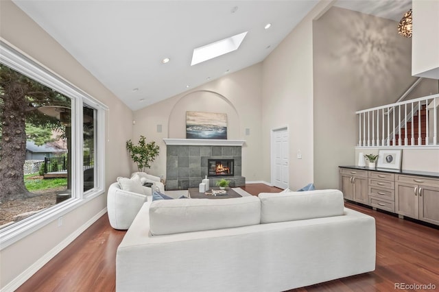 living room with high vaulted ceiling, a fireplace, a skylight, dark wood-type flooring, and baseboards
