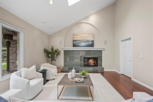 living room featuring wood finished floors, a tiled fireplace, baseboards, vaulted ceiling, and recessed lighting