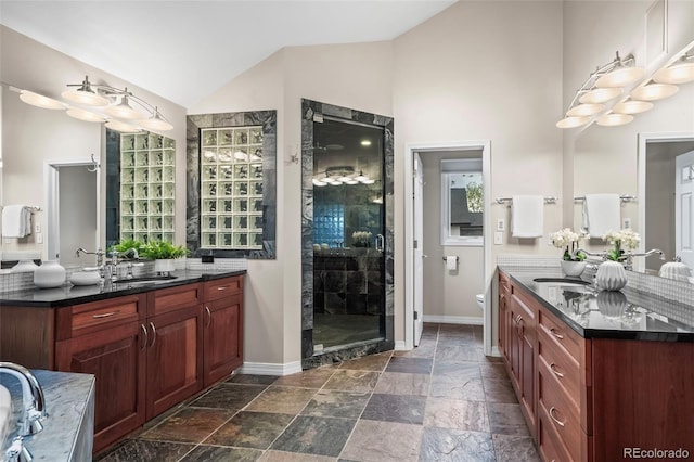 bathroom with lofted ceiling, a stall shower, stone tile flooring, baseboards, and a sink
