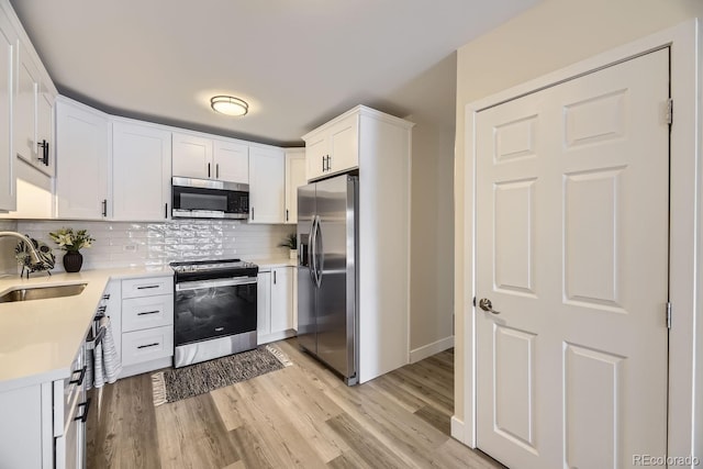 kitchen featuring sink, appliances with stainless steel finishes, white cabinetry, tasteful backsplash, and light wood-type flooring