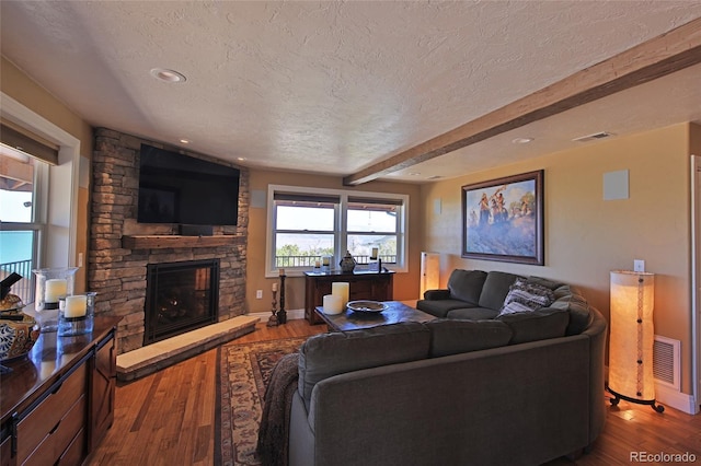 living area featuring beam ceiling, a textured ceiling, visible vents, a stone fireplace, and dark wood-type flooring