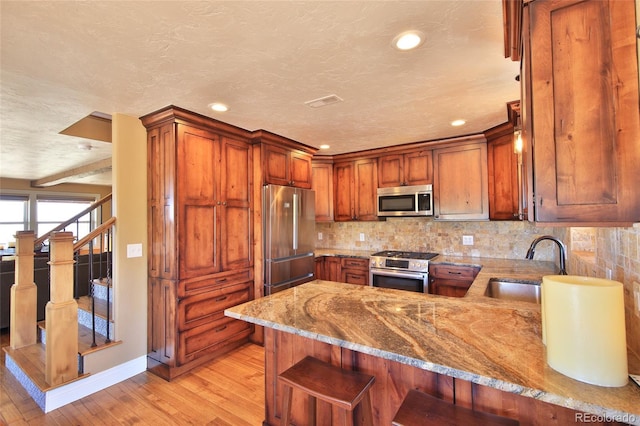kitchen with light stone counters, a sink, light wood finished floors, a peninsula, and appliances with stainless steel finishes
