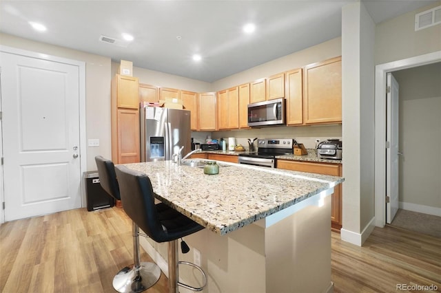 kitchen with light hardwood / wood-style floors, stainless steel appliances, and a center island with sink