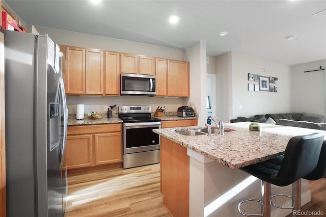 kitchen with light brown cabinets, light wood-type flooring, a kitchen breakfast bar, appliances with stainless steel finishes, and light stone countertops