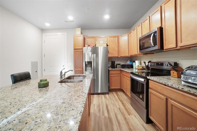 kitchen featuring a kitchen breakfast bar, sink, light wood-type flooring, light stone counters, and stainless steel appliances