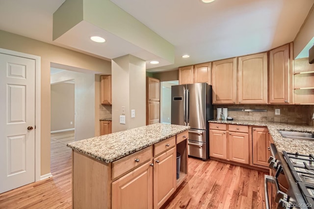 kitchen with sink, light wood-type flooring, decorative backsplash, light stone counters, and stainless steel fridge