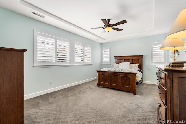 bedroom with ceiling fan, a tray ceiling, and light colored carpet