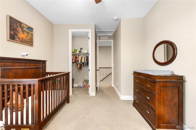 bedroom featuring ceiling fan, a nursery area, light carpet, a spacious closet, and a closet